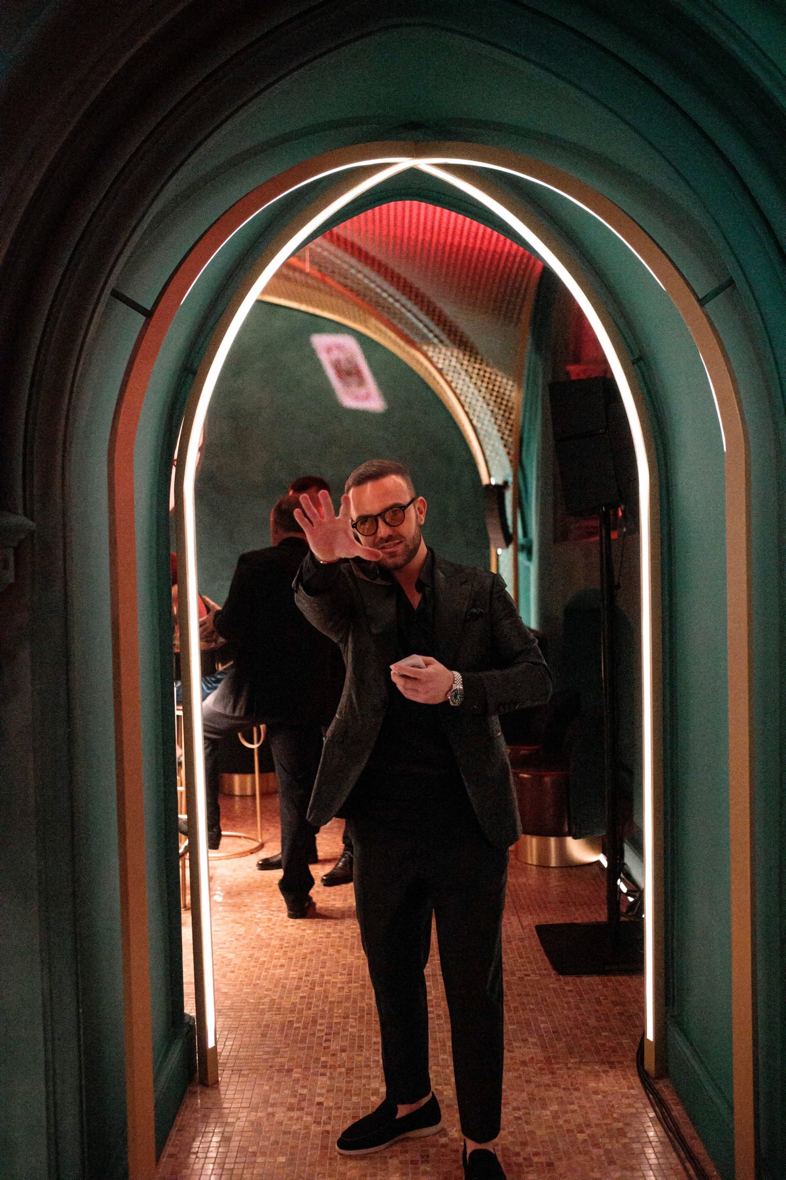 Matteo Cammisa under a lit archway, a single playing card frozen in the air above him.
